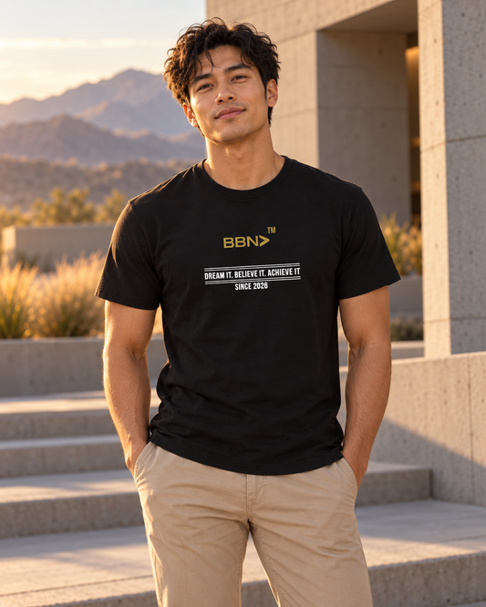 AI styling concept: Man outdoors wearing a black T-shirt with white “Dream It Believe It Achieve It” lettering and a gold BBN logo.