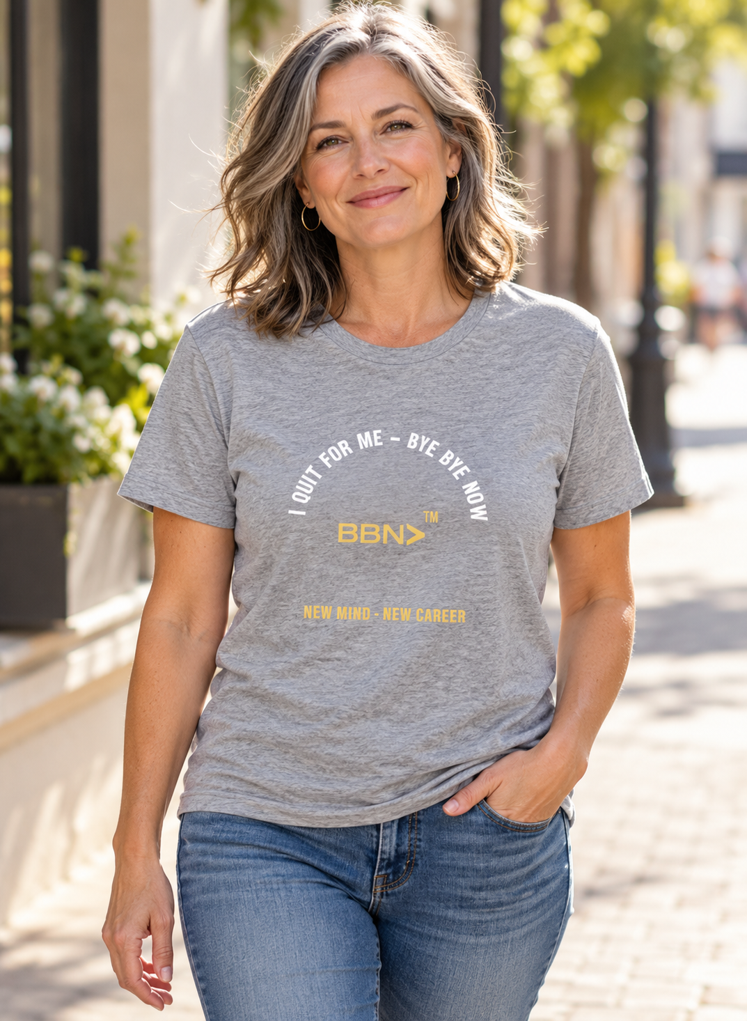 AI styling concept: Woman outdoors wearing an athletic heather gray T-shirt with white “I Quit For Me – Bye Bye Now” lettering and a gold BBN logo.