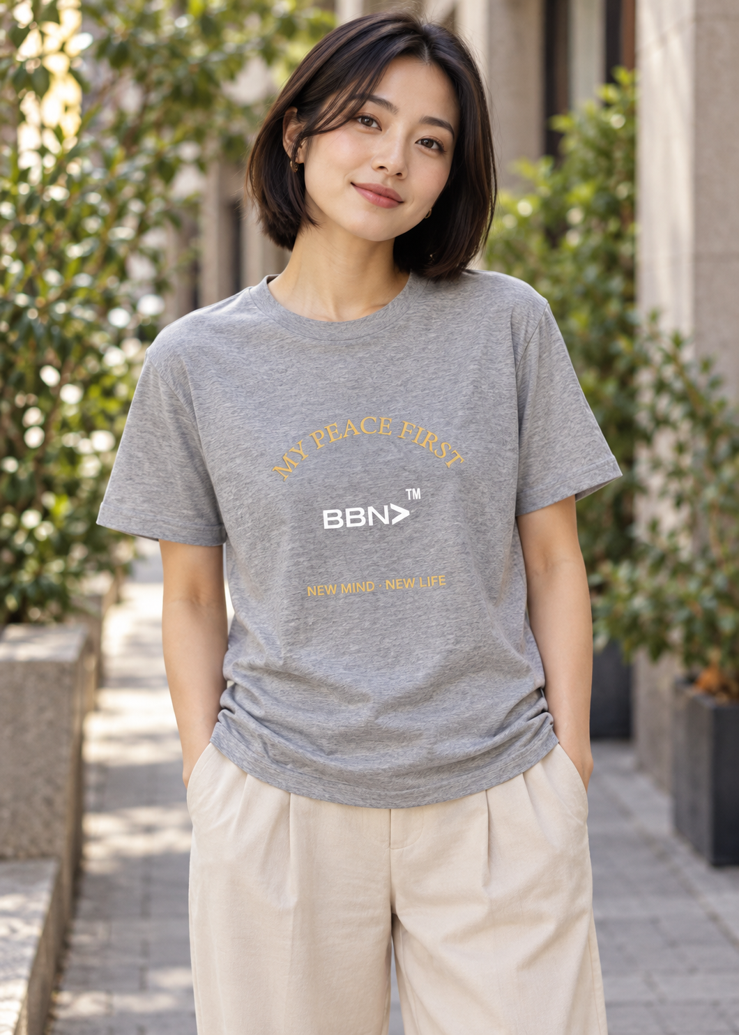 AI styling concept: Woman outdoors wearing an athletic heather gray T-shirt with gold “My Peace First” lettering and a white BBN logo.