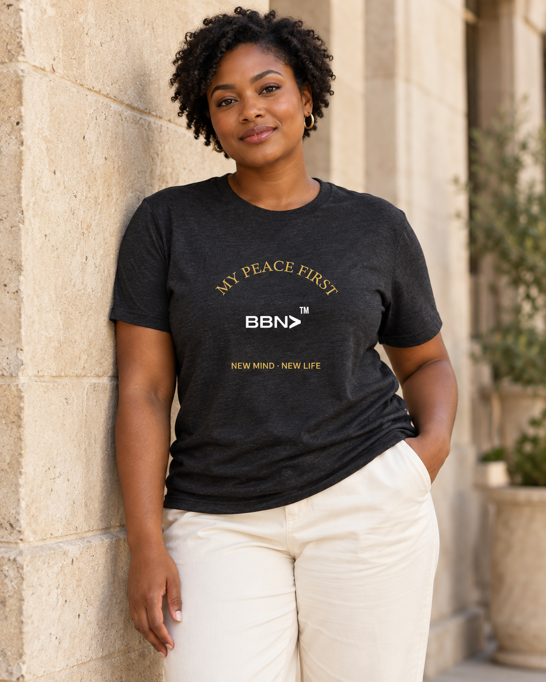 AI styling concept: Woman outdoors wearing a black heather T-shirt with gold “My Peace First” lettering and a white BBN logo.