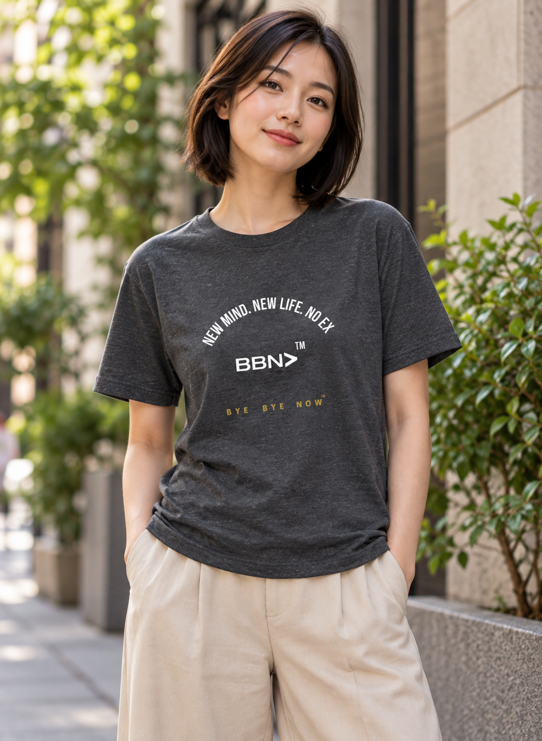 AI styling concept: Woman outdoors wearing a dark gray heather T-shirt with white “New Mind New Life No Ex” lettering and a white BBN logo.