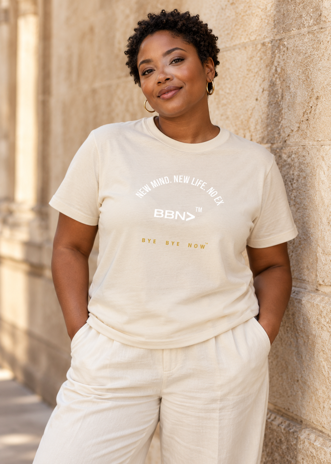 AI styling concept: Woman outdoors wearing a natural cream T-shirt with white “New Mind New Life No Ex” lettering and a white BBN logo.