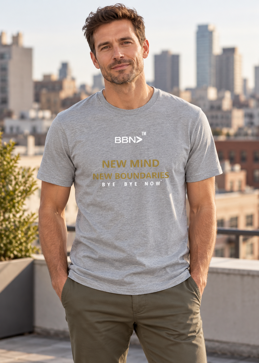AI styling concept: Man outdoors wearing an athletic heather gray T-shirt with gold “New Mind New Boundaries” lettering and a white BBN logo.