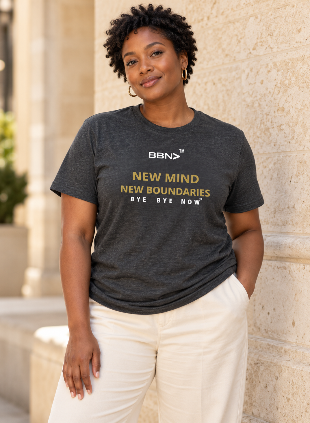 AI styling concept: Woman outdoors wearing a dark gray heather T-shirt with gold “New Mind New Boundaries” lettering and a white BBN logo.