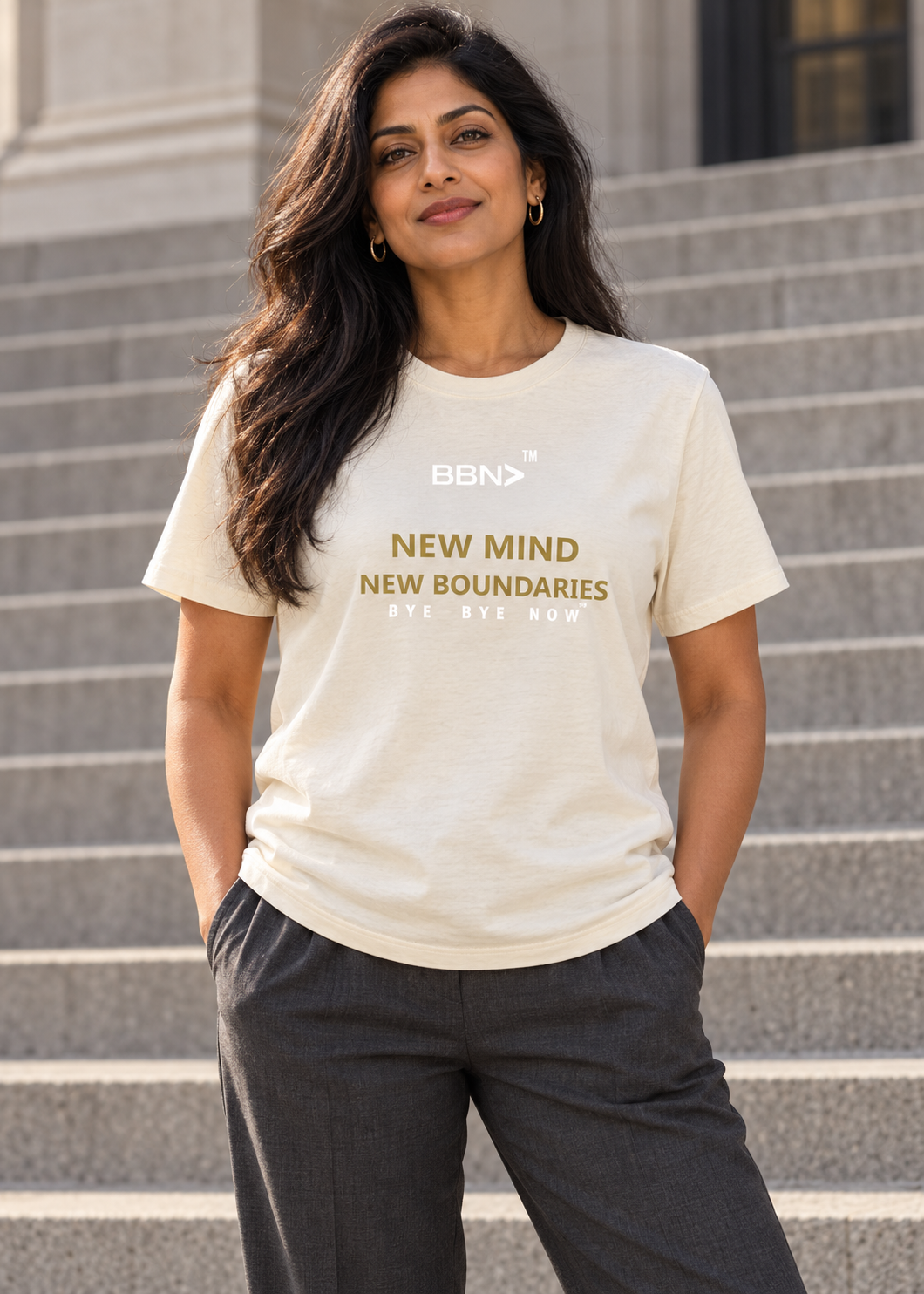 AI styling concept: Woman outdoors wearing a natural cream T-shirt with gold “New Mind New Boundaries” lettering and a white BBN logo.