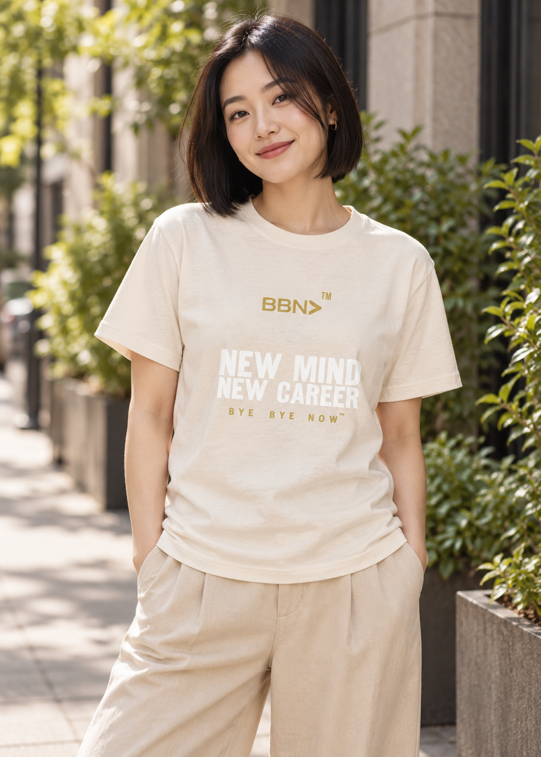AI styling concept: Woman outdoors wearing a natural cream T-shirt with white “New Mind New Career” lettering and a gold BBN logo.