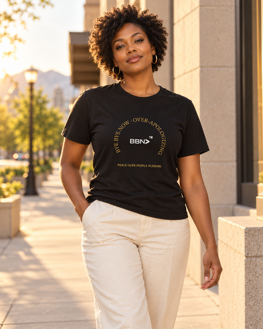 AI styling concept: Woman outdoors wearing a black T-shirt with gold “Over-Apologizing” lettering around a white BBN logo.
