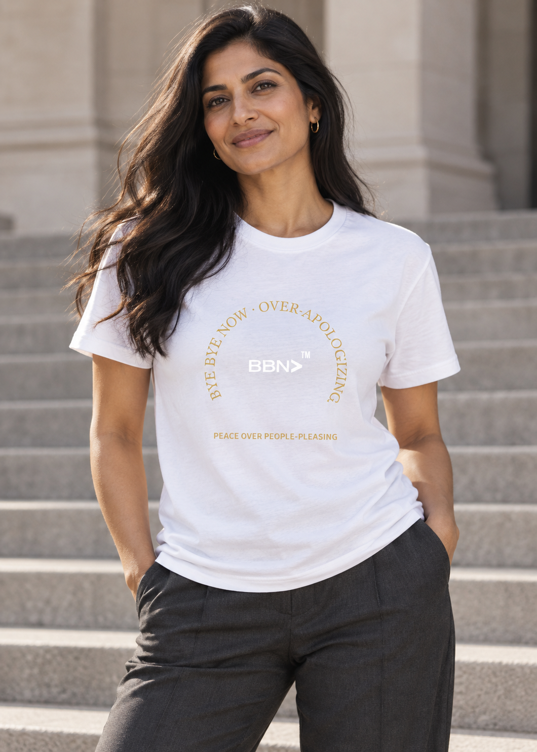 AI styling concept: Woman outdoors wearing a white T-shirt with gold “Over-Apologizing” lettering around a white BBN logo.
